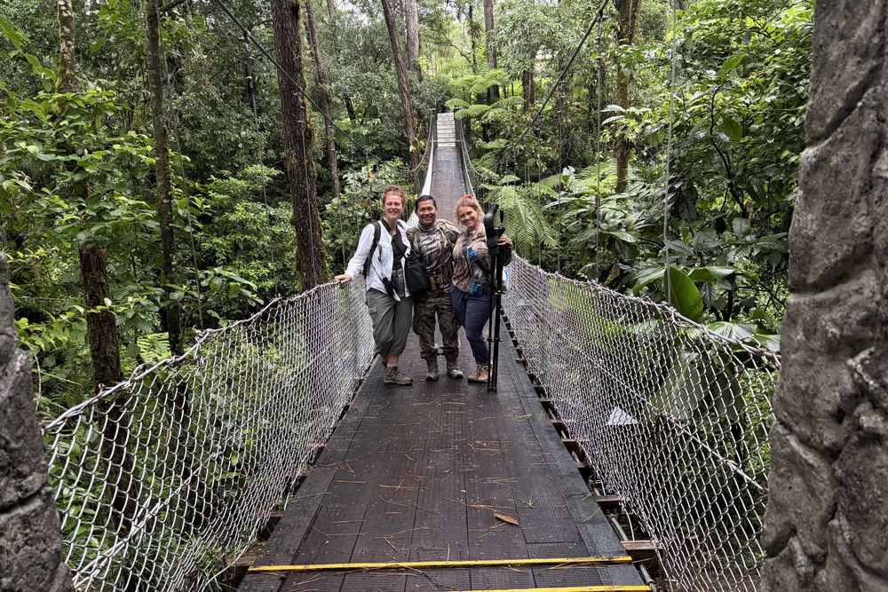 Maleku with Tasha and a friend on a suspension bridge through the rainforest canopy, spotting scope on his shoulder