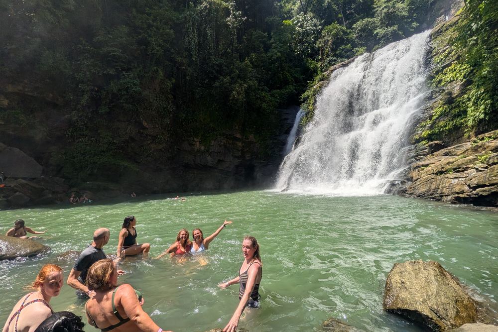 Nauyaca Waterfalls dropping into a wide green pool, swimmers in the shallows below