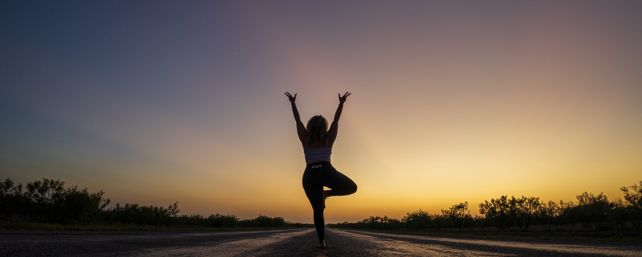 A figure in tree pose on an empty road at sunset