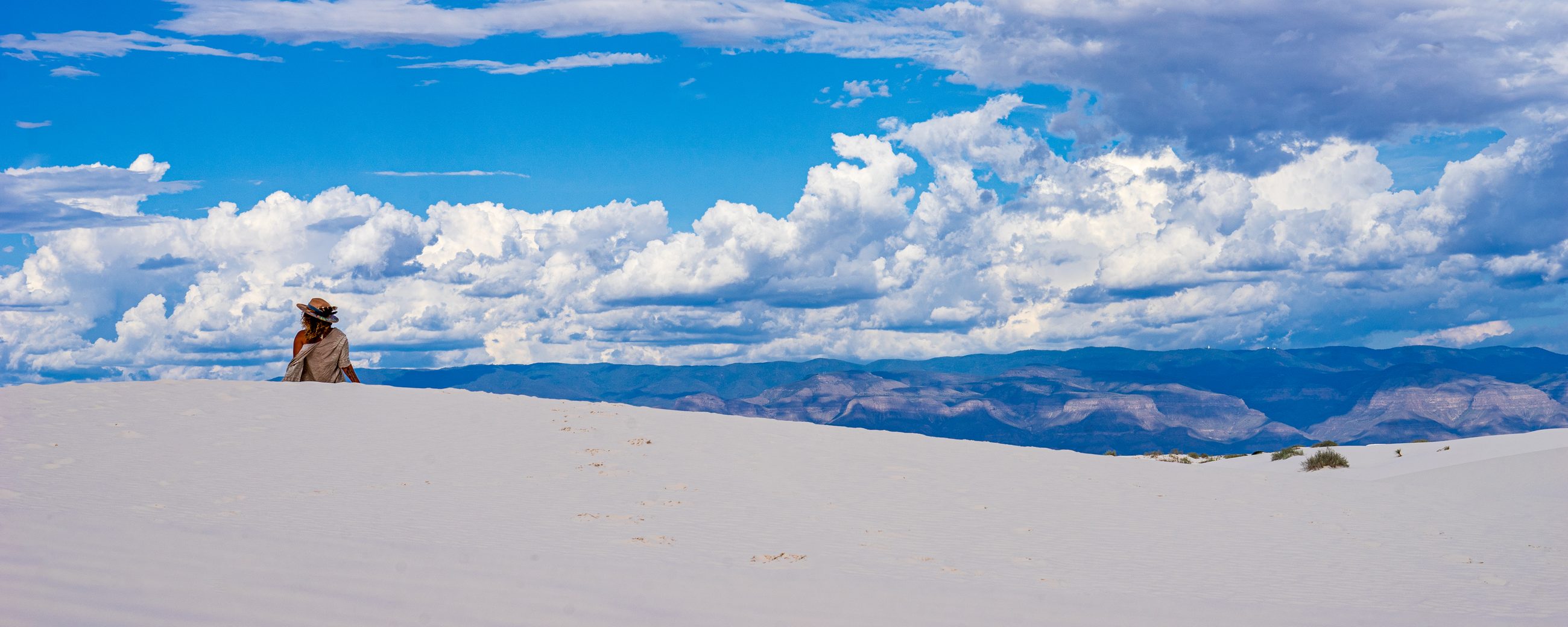 A wide, open landscape of pale sand and rock under a bright sky