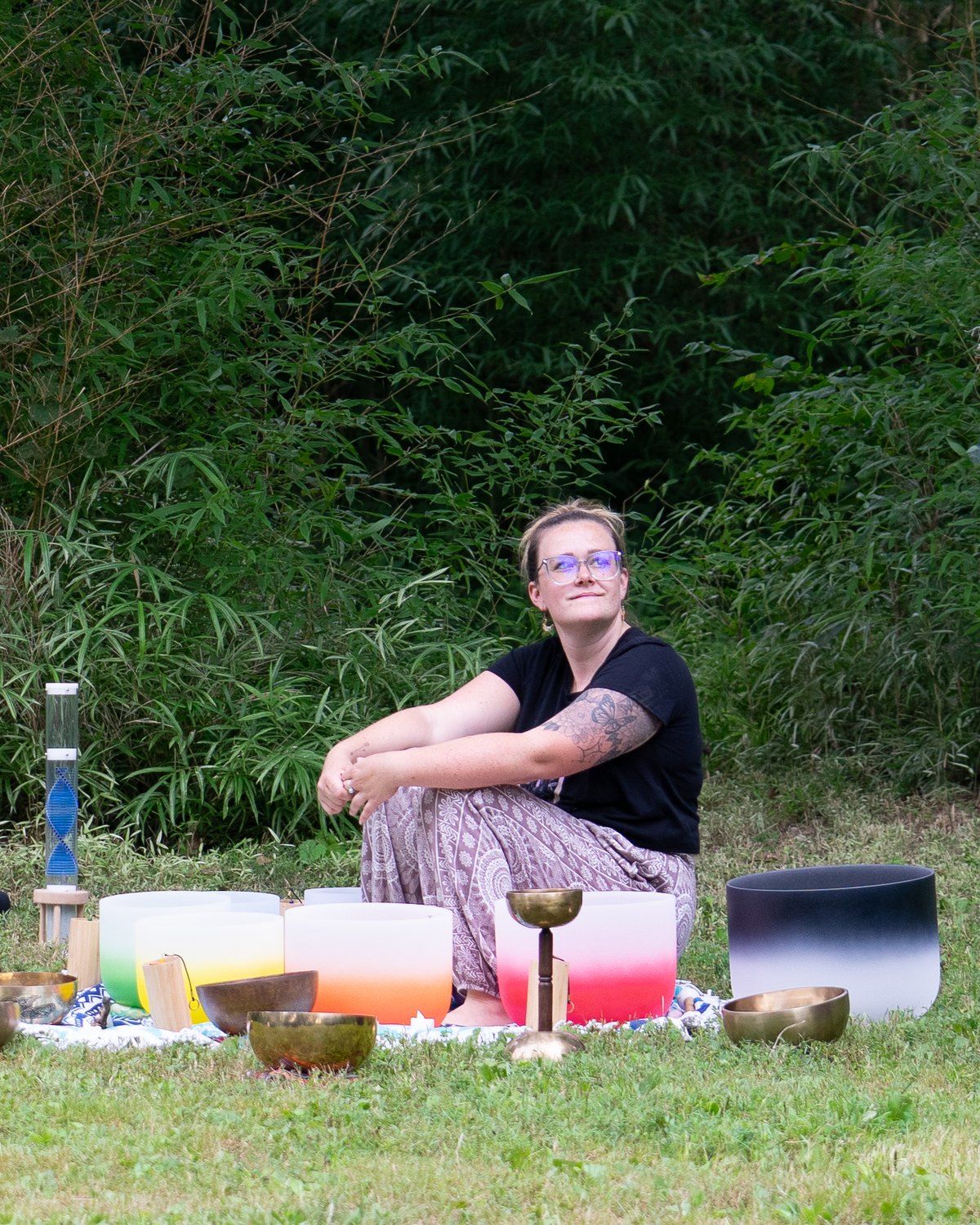 Kelly Fisher seated among crystal singing bowls at an outdoor session in the bamboo grove