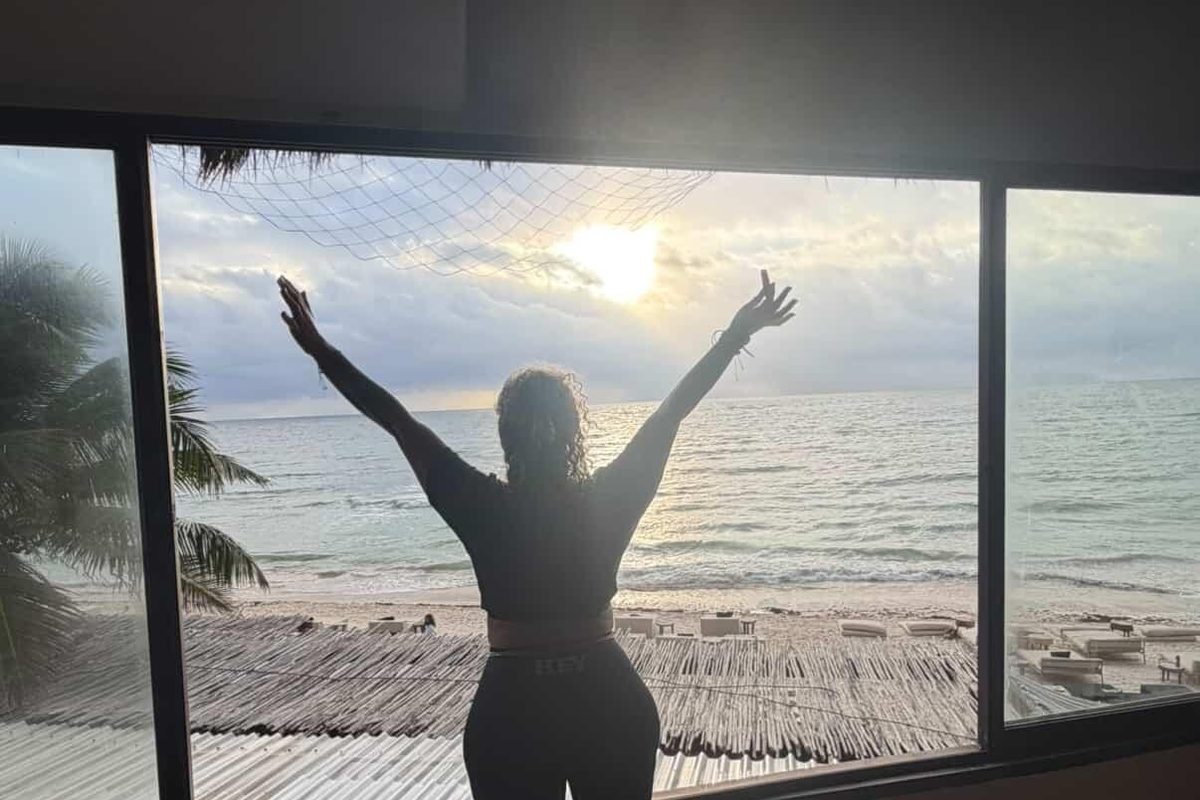 A silhouette with both arms raised in front of a sunrise over the sea